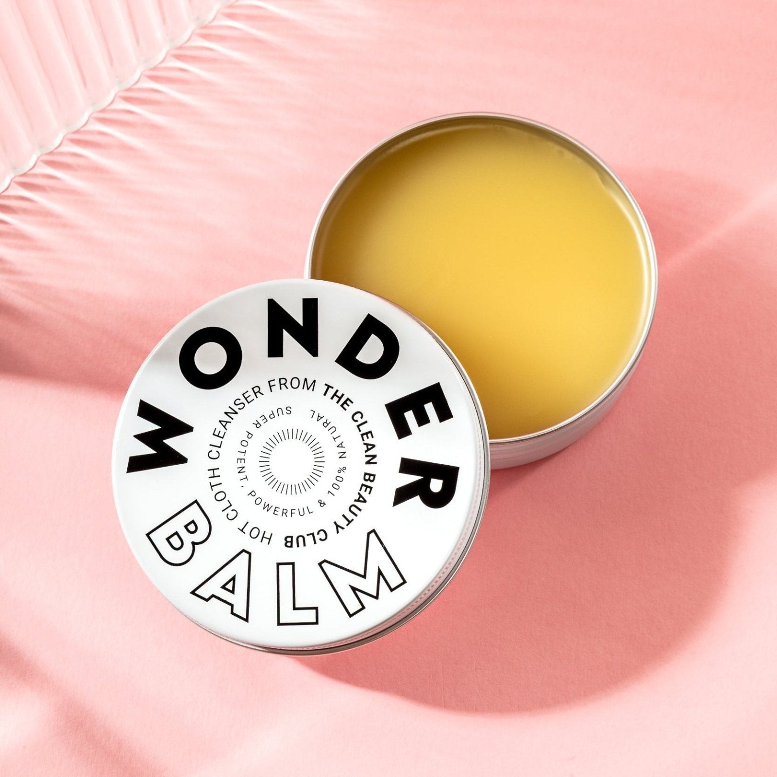Wonder Balm container with yellow balm on a pink background