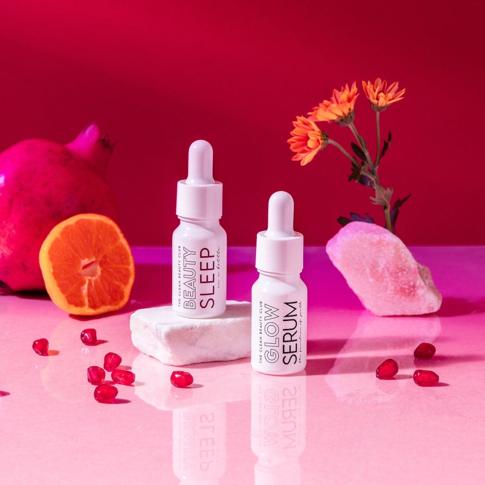 Two skincare serum bottles labeled 'Beauty Sleep' and 'Glow Serum' on a pink surface with decorative elements.