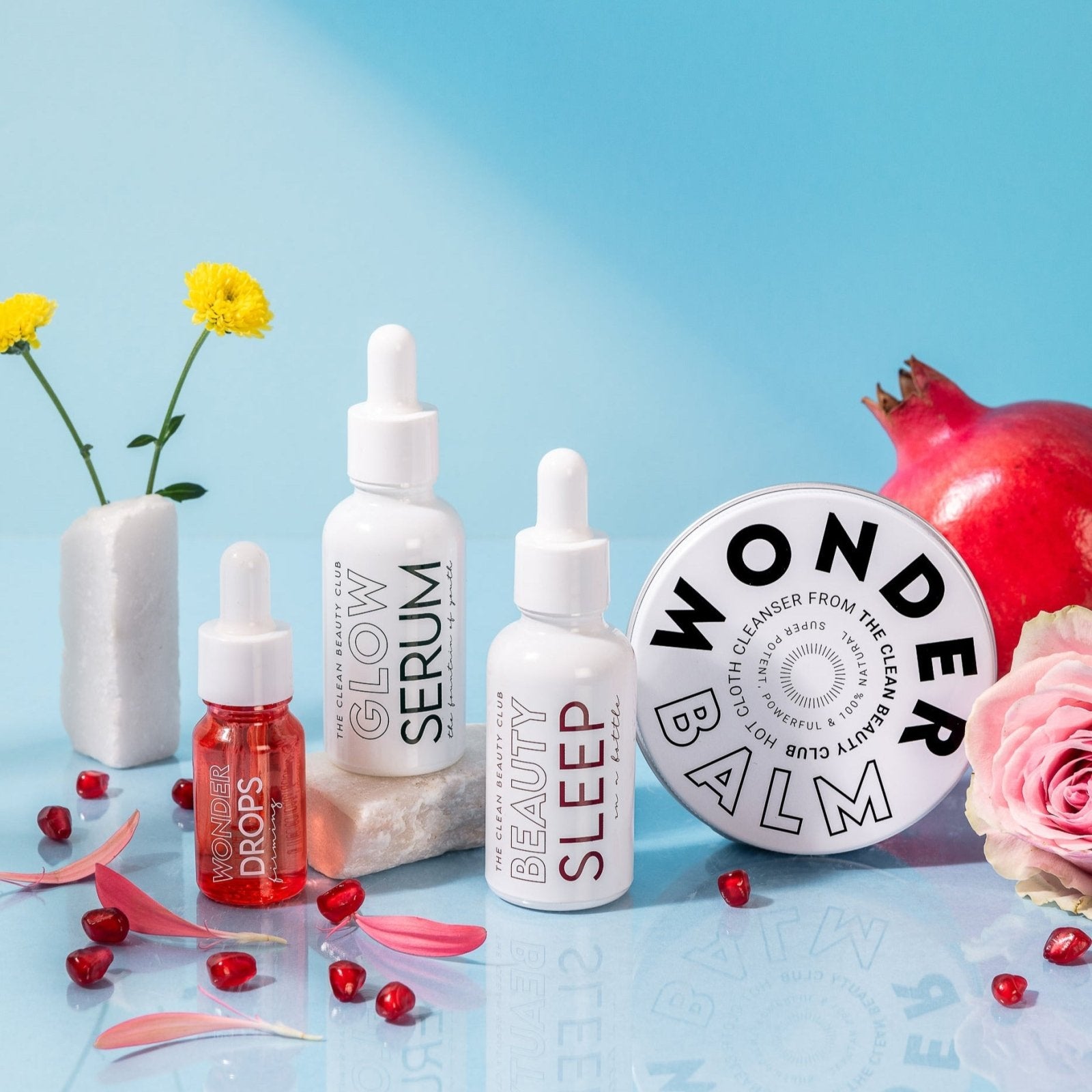 Collection of skincare products including a balm, serum, and sleep drops on a blue background with flowers.