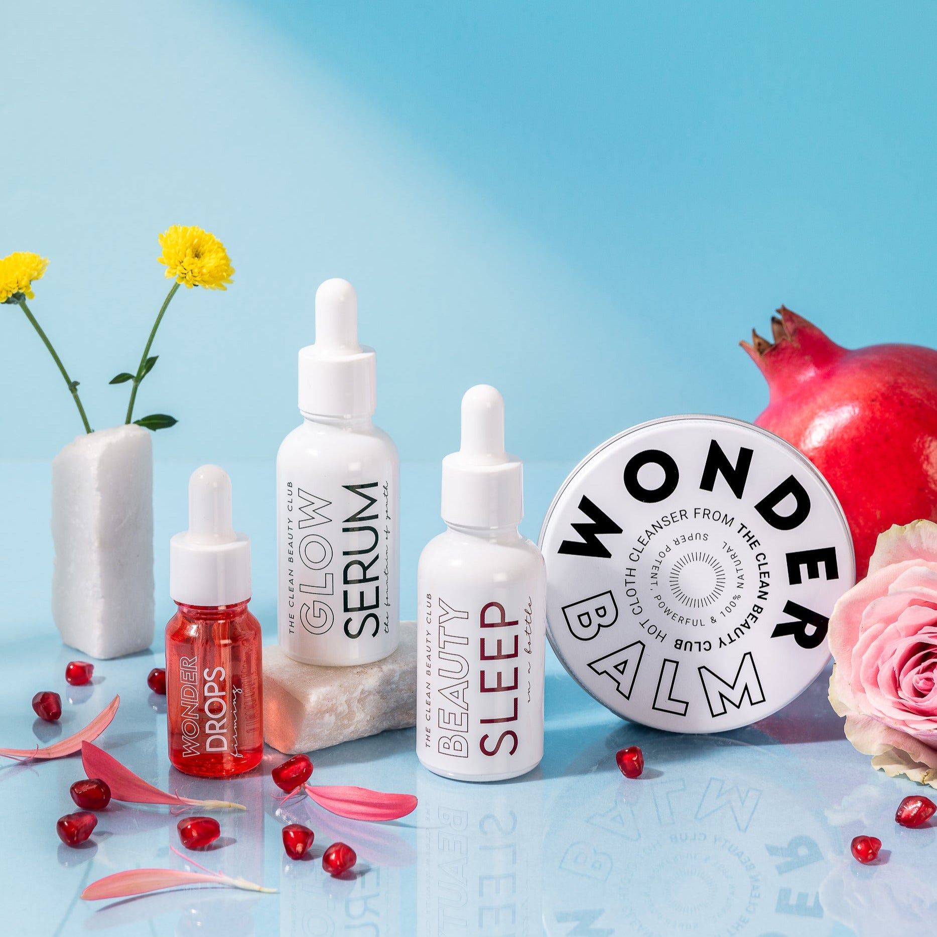 Collection of skincare products including a balm, serum, and sleep drops on a blue background with flowers.